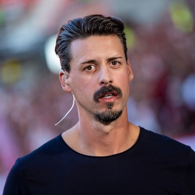Der ehemalige deutsche Fußball-Nationalspieler Sandro Wagner trägt ein Headset und steht vor einem Spiel im Stadion. Er blickt in die Kamera.
