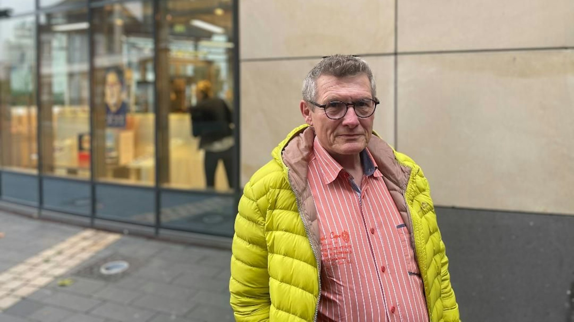 Michael Baum steht auf der Straße. Der Mann trägt eine gelbe Jacke und ein rotes Hemd.