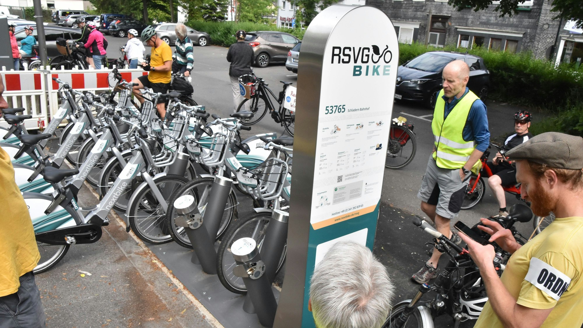 Menschen stehen um eine Stele der RSVG Bike-Vermietung herum. Dahinter sind E-Bikes aufgestellt.