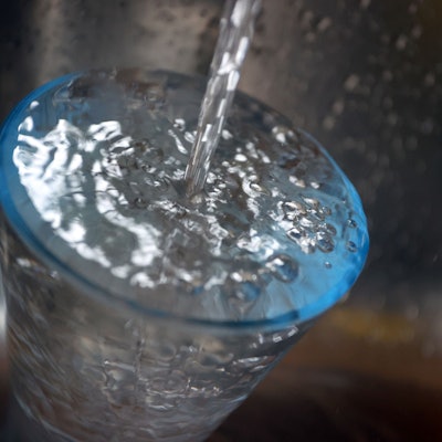 Leitungswasser fließt in ein Glas, das in einem Spülbecken steht. Der Versorger Belkaw fordert die Bürger von Bergisch Gladbach auf, sparsam mit Wasser umzugehen.