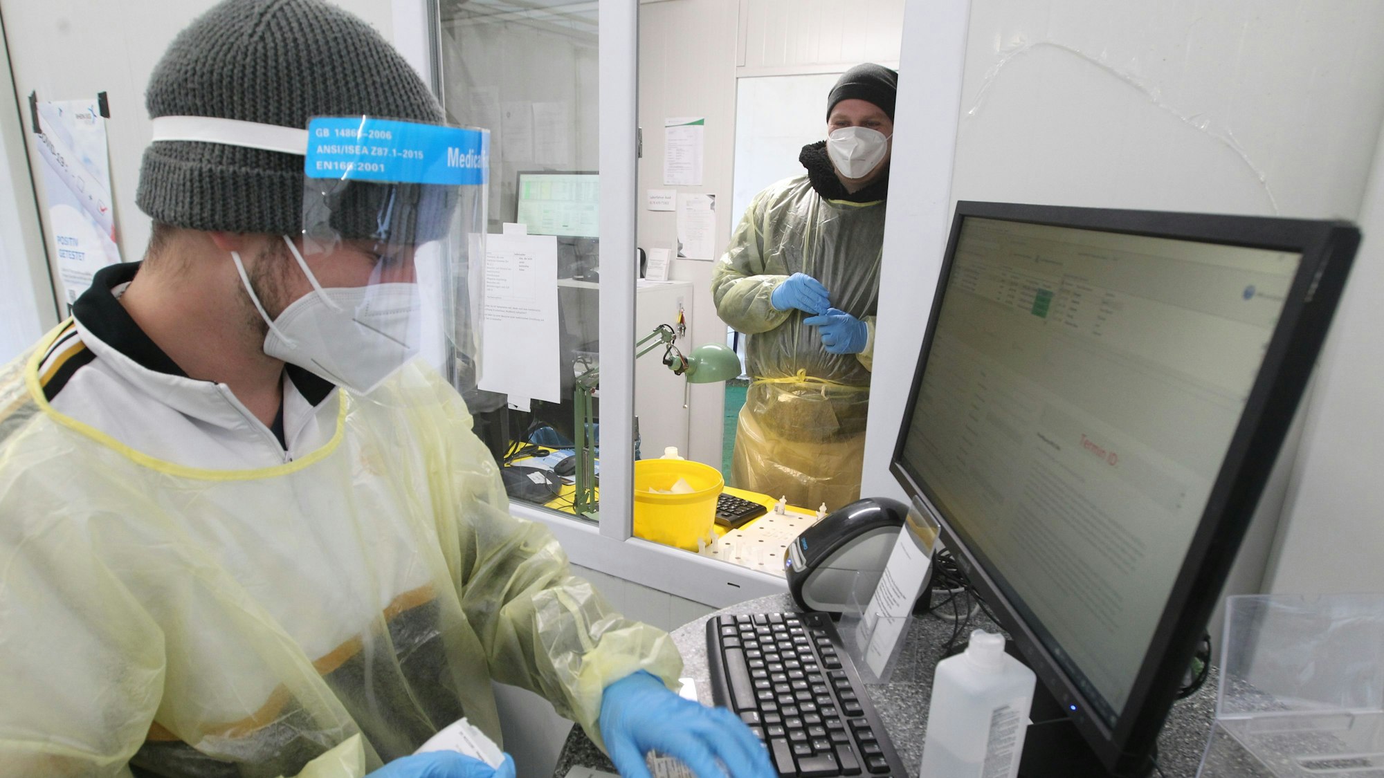 Ein Mitarbeiter im Lohmarer Testzentrum arbeitet an einem Computer in Schutzanzug, mit FFP-2-Maske und Gesichtsschild.