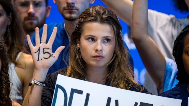 Klimaaktivistin Luisa Neubauer von „Fridays for Future“ hält eine Hand hoch, auf der „1,5 Grad“ geschrieben steht. Neubauer blickt ernst nach vorne.