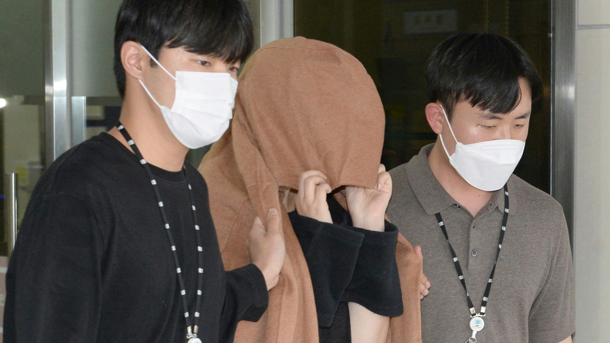 Eine Frau (Mitte) verlässt die Staatsanwaltschaft des zentralen Bezirks Seoul in der Polizeistation Ulsan Jungbu. Sie verdeckt ihren Kopf mit einem braunen Tuch. Zwei Männer führen sie aus dem Gebäude.