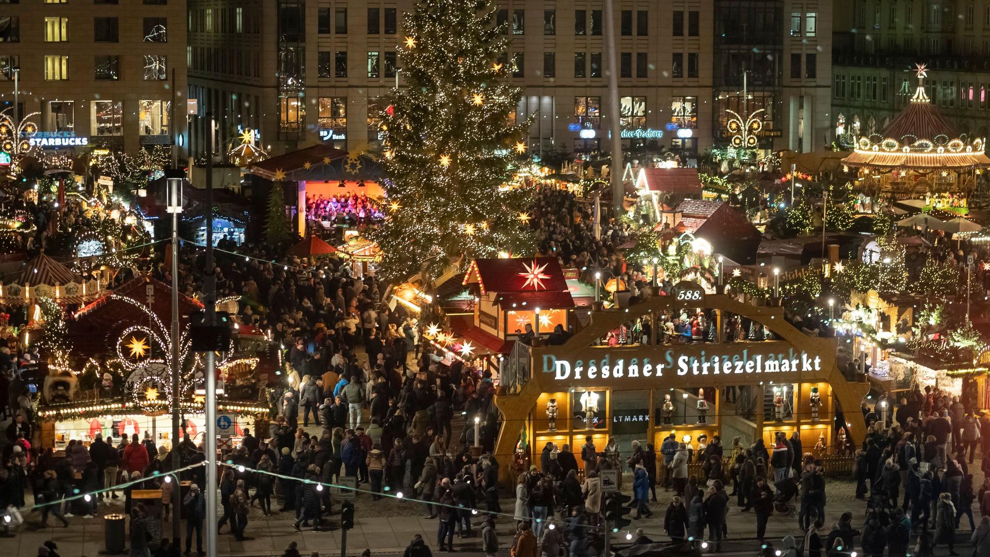 Besucher laufen zwischen festlich dekorierten Ständen und Weihnachtsbäumen über den Weihnachtsmarkt in Dresden.