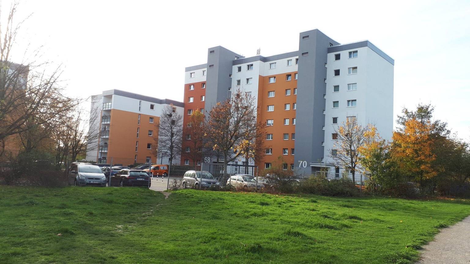 Ein grau-orangefarbener Wohnblock steht am Rande einer Rasenfläche.