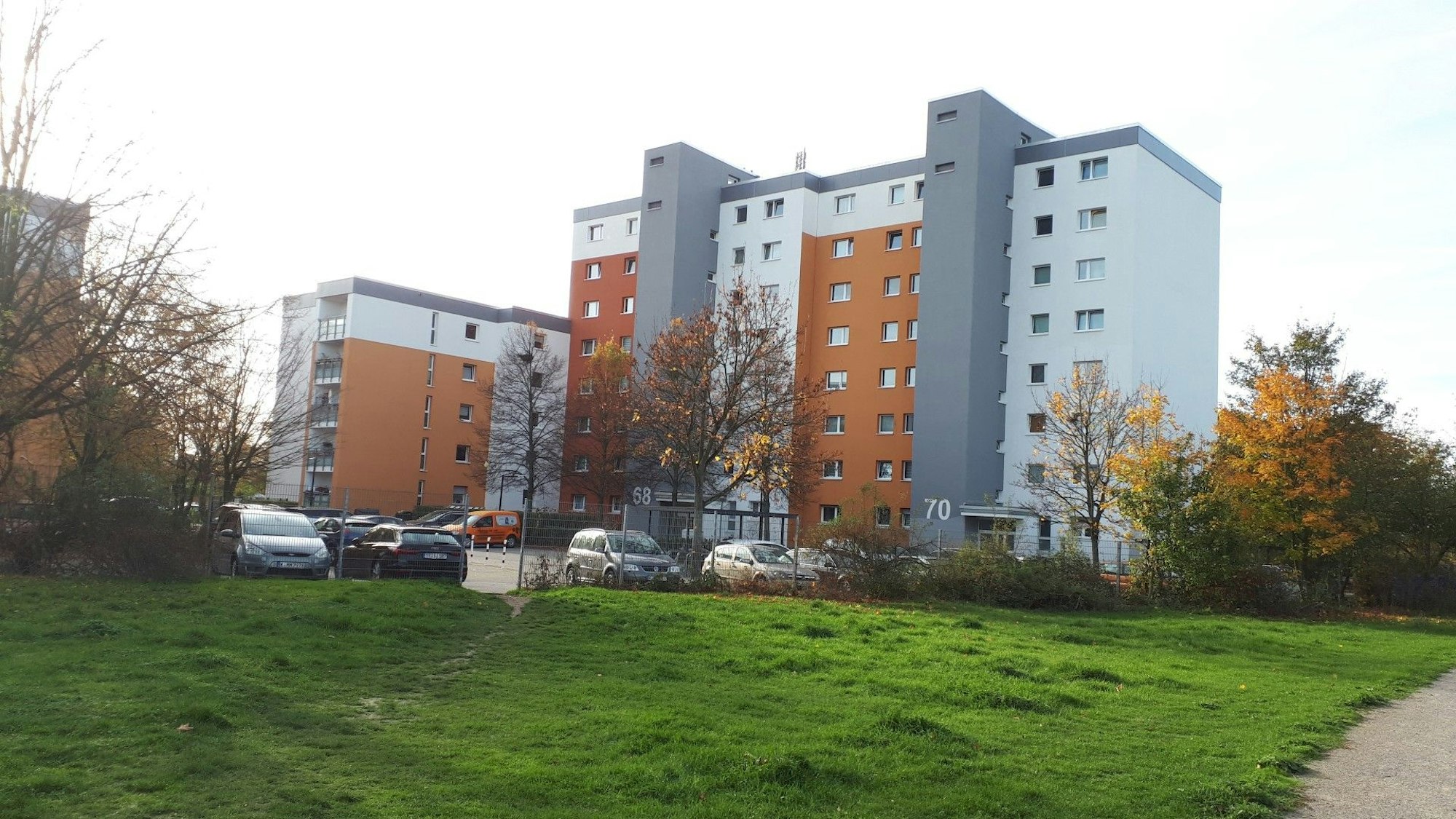 Ein grau-orangefarbener Wohnblock steht am Rande einer Rasenfläche.