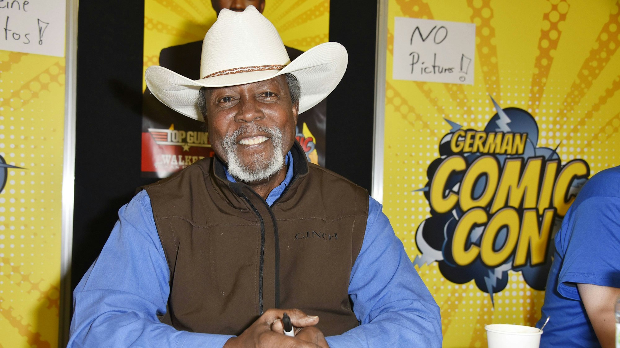 Clarence Gilyard Jr. auf der 4. German Comic Con Dortmund 2018 in den Westfalenhallen. Er trägt einen hellen Cowboy-Hut, hat einen Edding in den Händen und lächelt in die Kamera.