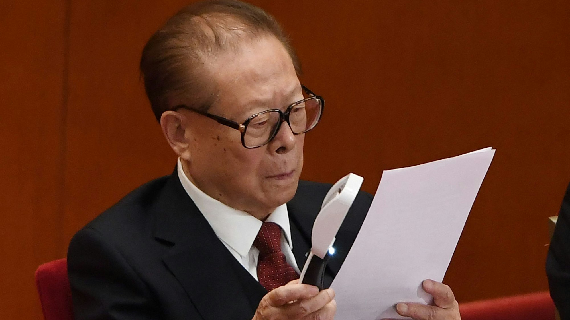 Der frühere chinesische Präsident, Jiang Zemin, liest auf einem Parteitag einen Bericht mithilfe einer Lupe.