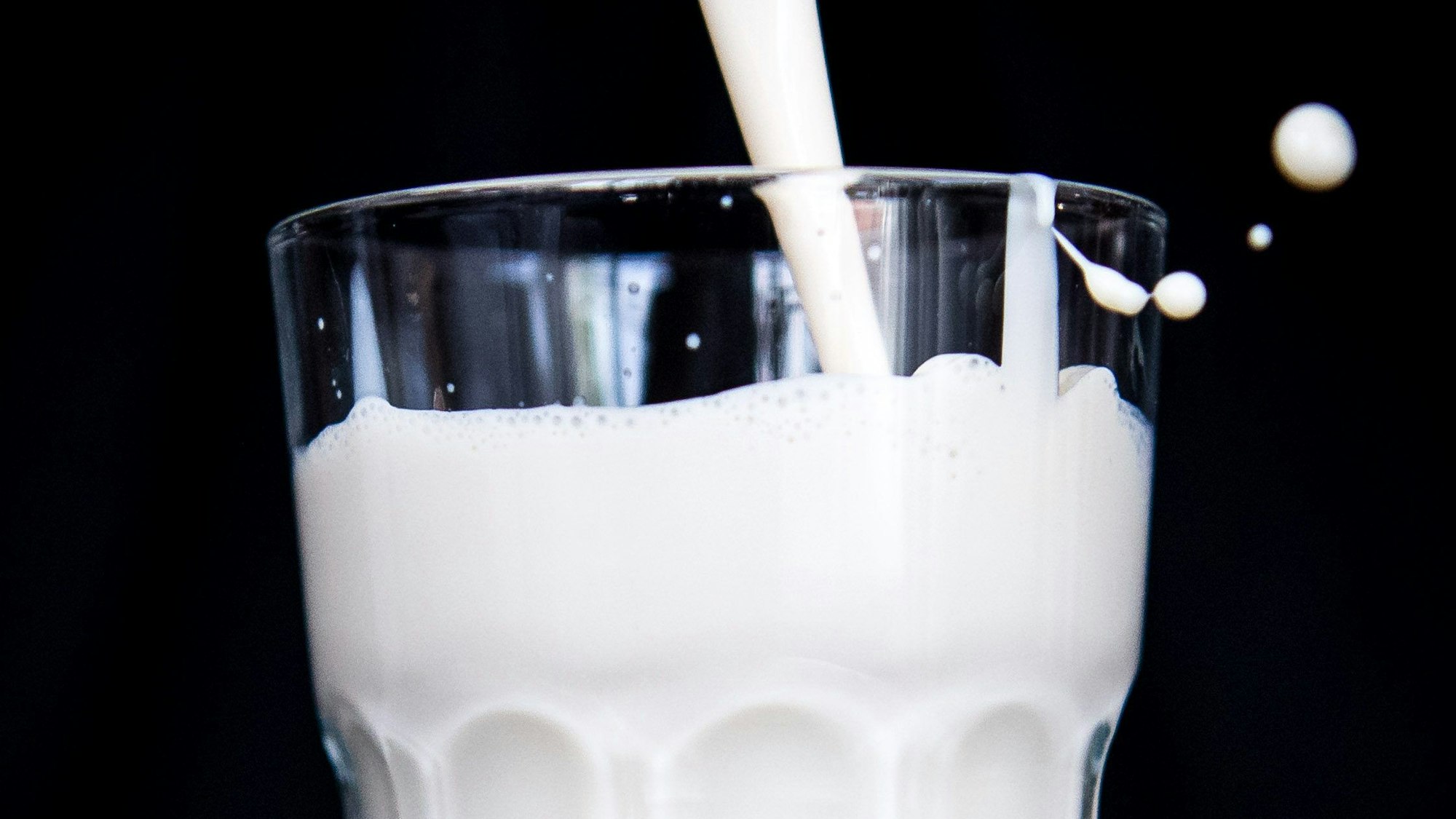 Hafermilch wird in ein Glas geschüttet. Die weiße Milch schäumt beim Kippen leicht und spritzt über den Glasrand hinaus. (Symbolbild)