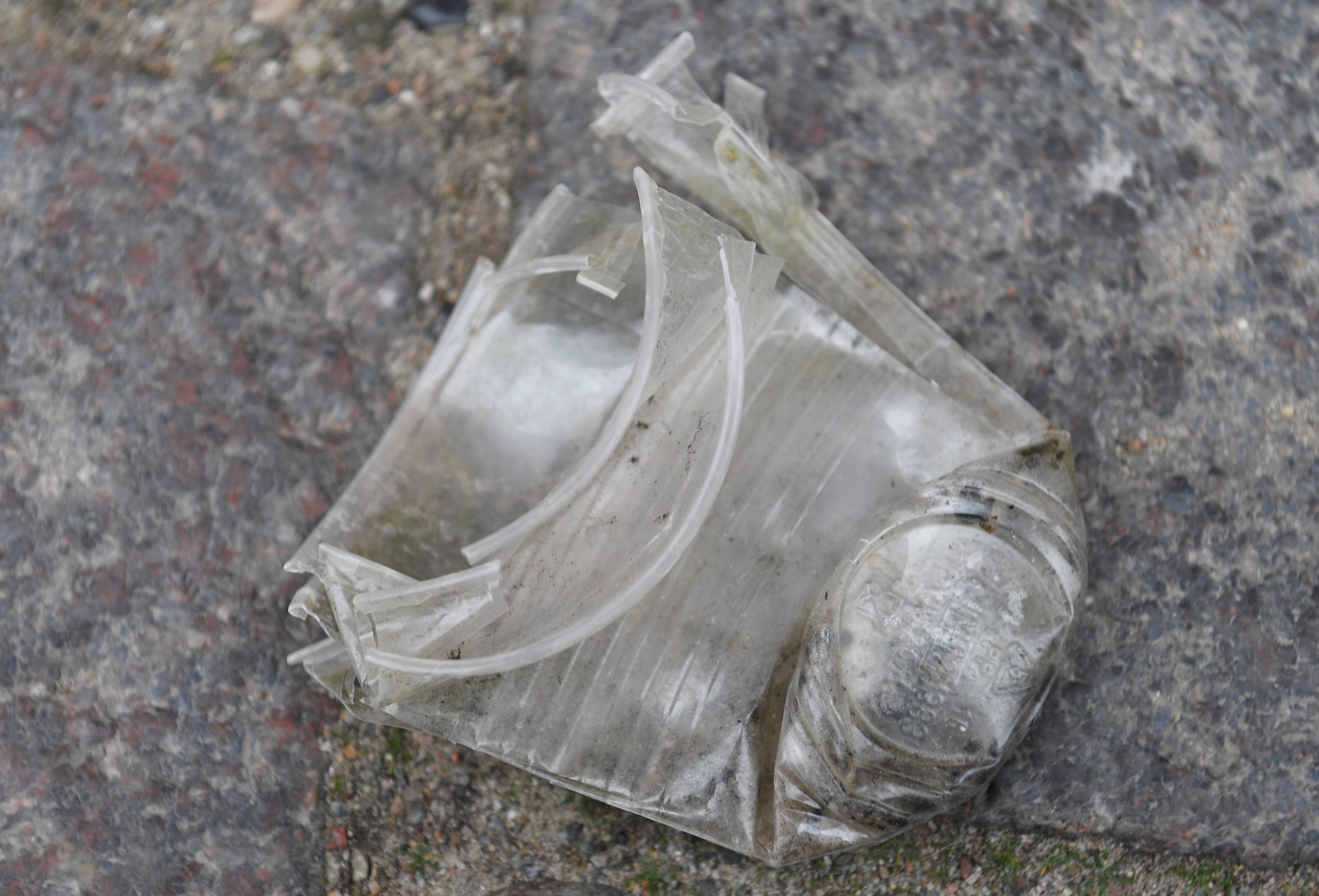 Ein zerknüllter und dreckiger Plastikbecher liegt auf einer Straße.