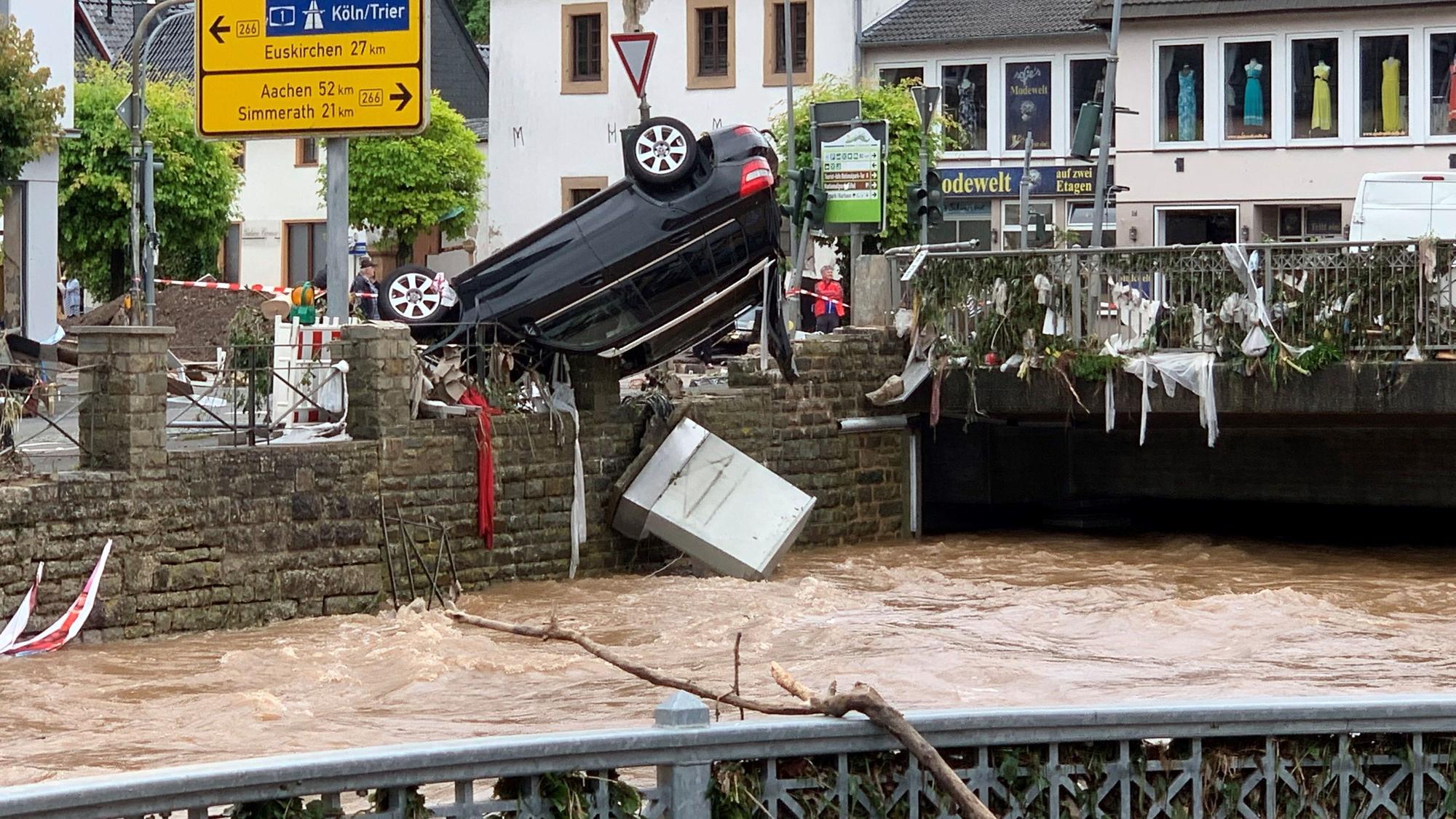 Nach dem Hochwasser am 14. Juli 2021 hängt ein Auto kopfüber an einem Geländer in Gemünd.