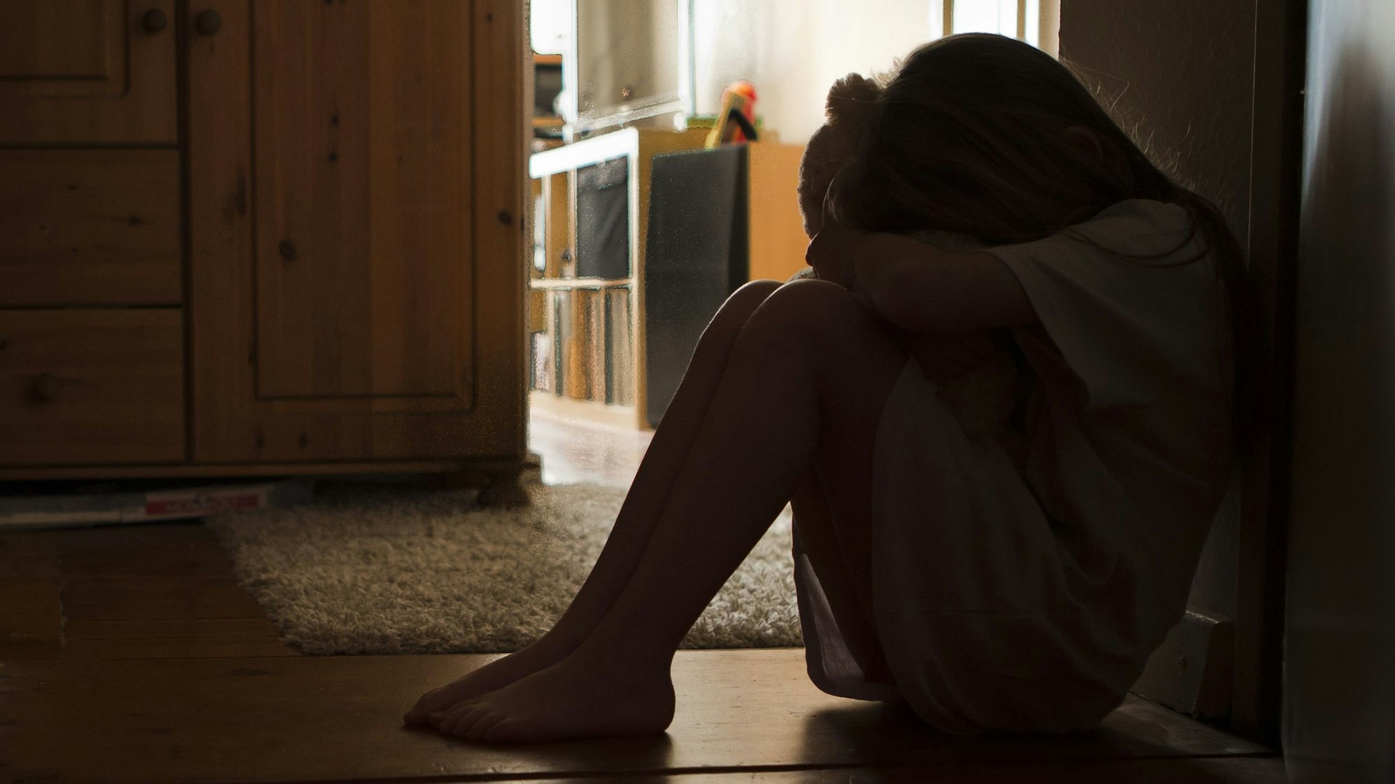 Ein Kind sitzt auf dem Boden und drückt sein Gesicht in einen Teddy.