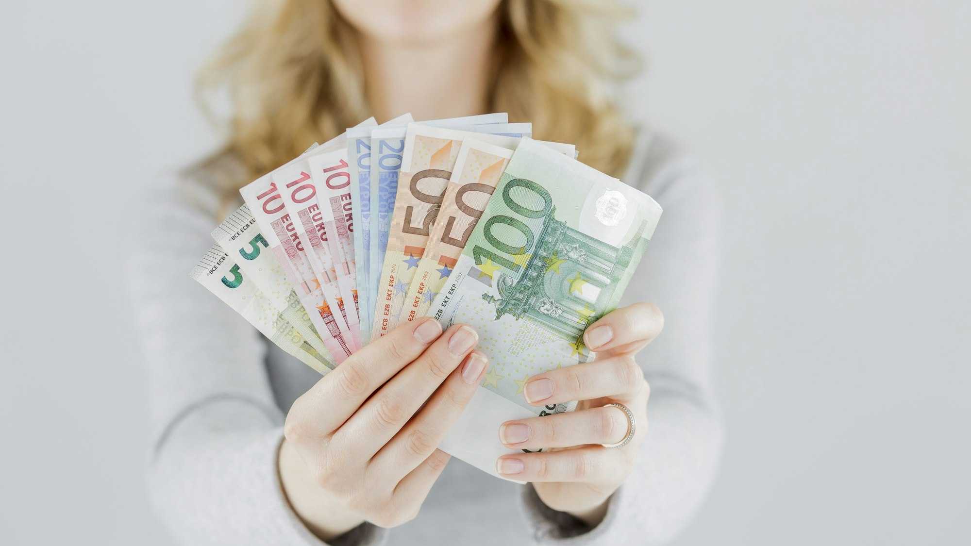 Eine junge Frau hält ein aufgefächertes Bündel Geldscheine in der Hand.