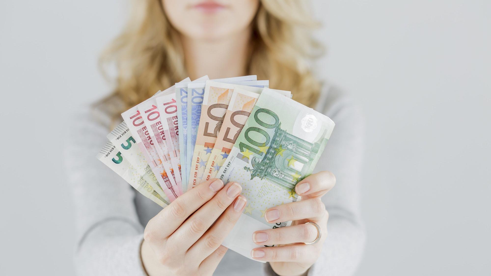 Eine Frau hält verschiedene Geldscheine in die Kamera, von fünf bis 100 Euro.
