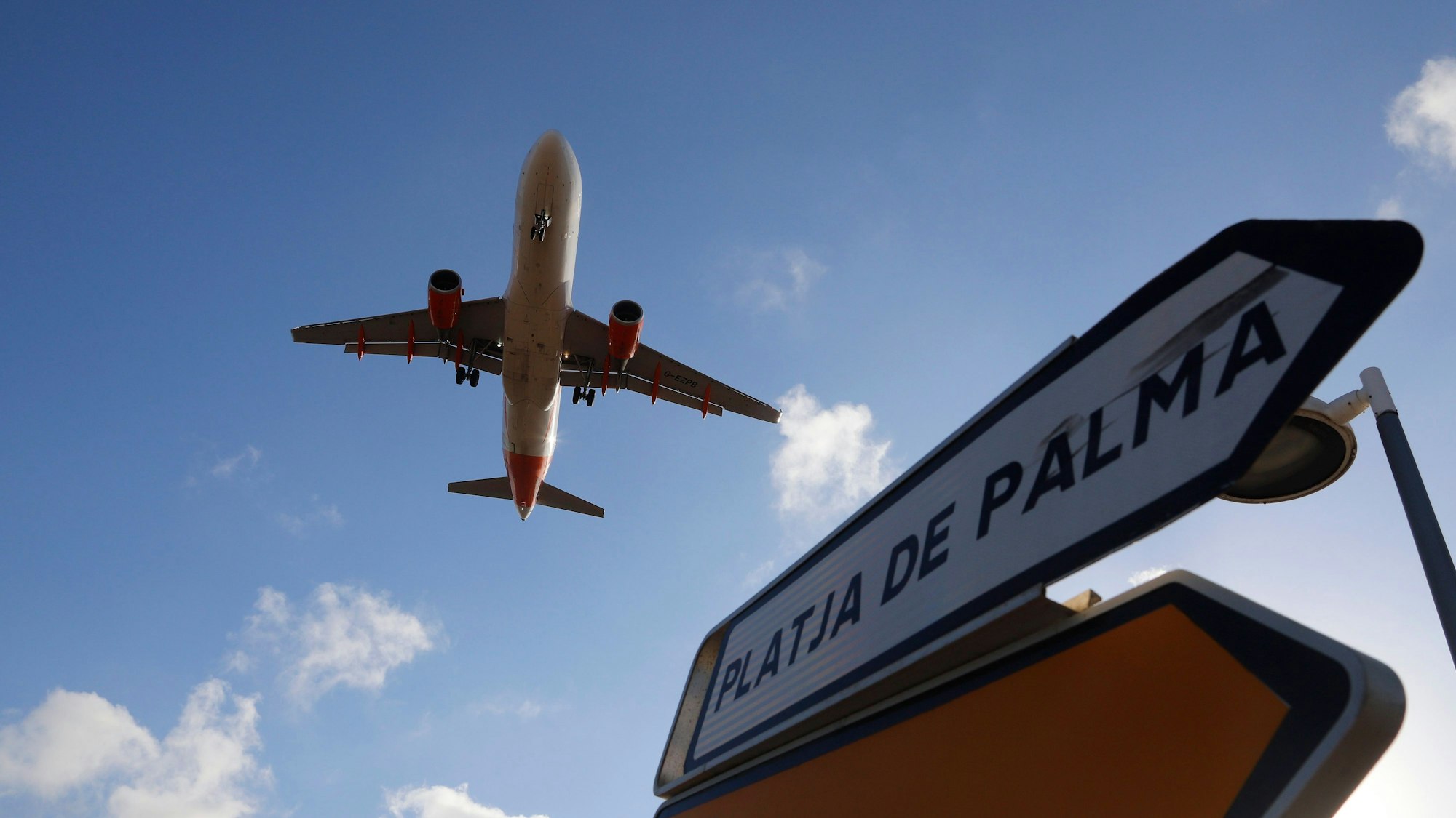 ARCHIV - 18.08.2020, Spanien, Palma: Ein Flugzeug überfliegt bei der Landung auf Mallorca ein Schild, das die Richtung nach Playa de Palma anzeigt.