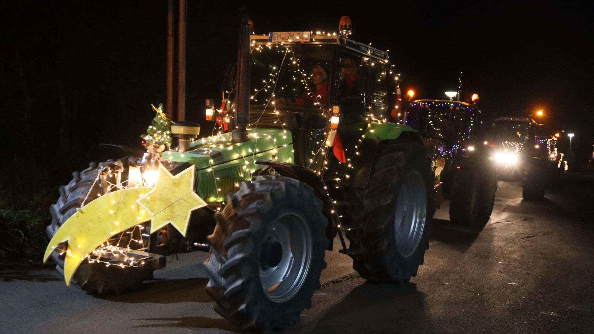 Weihnachtlich geschmückte Traktoren fahren in der Dunkelheit.