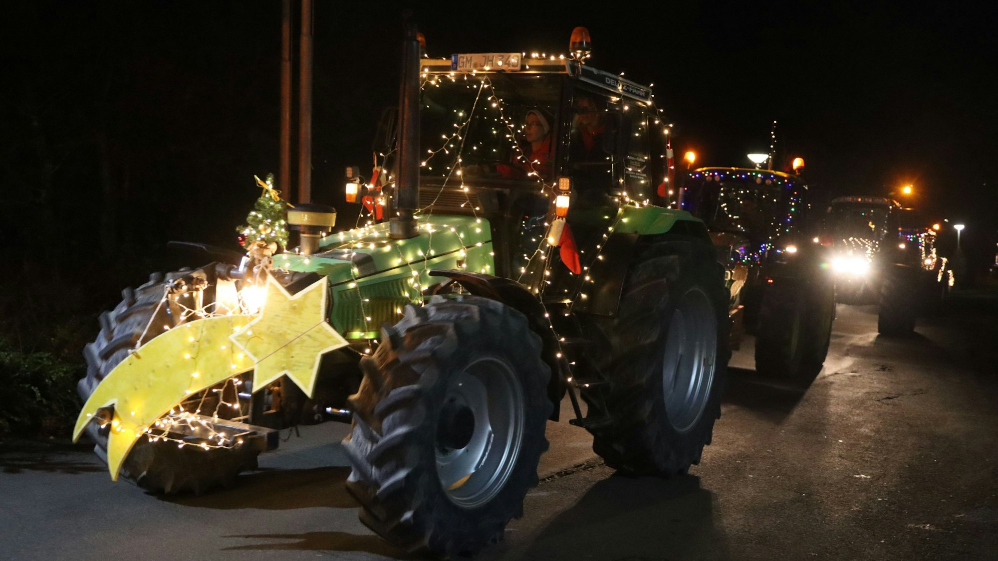 Weihnachtlich geschmückte Traktoren fahren in der Dunkelheit.