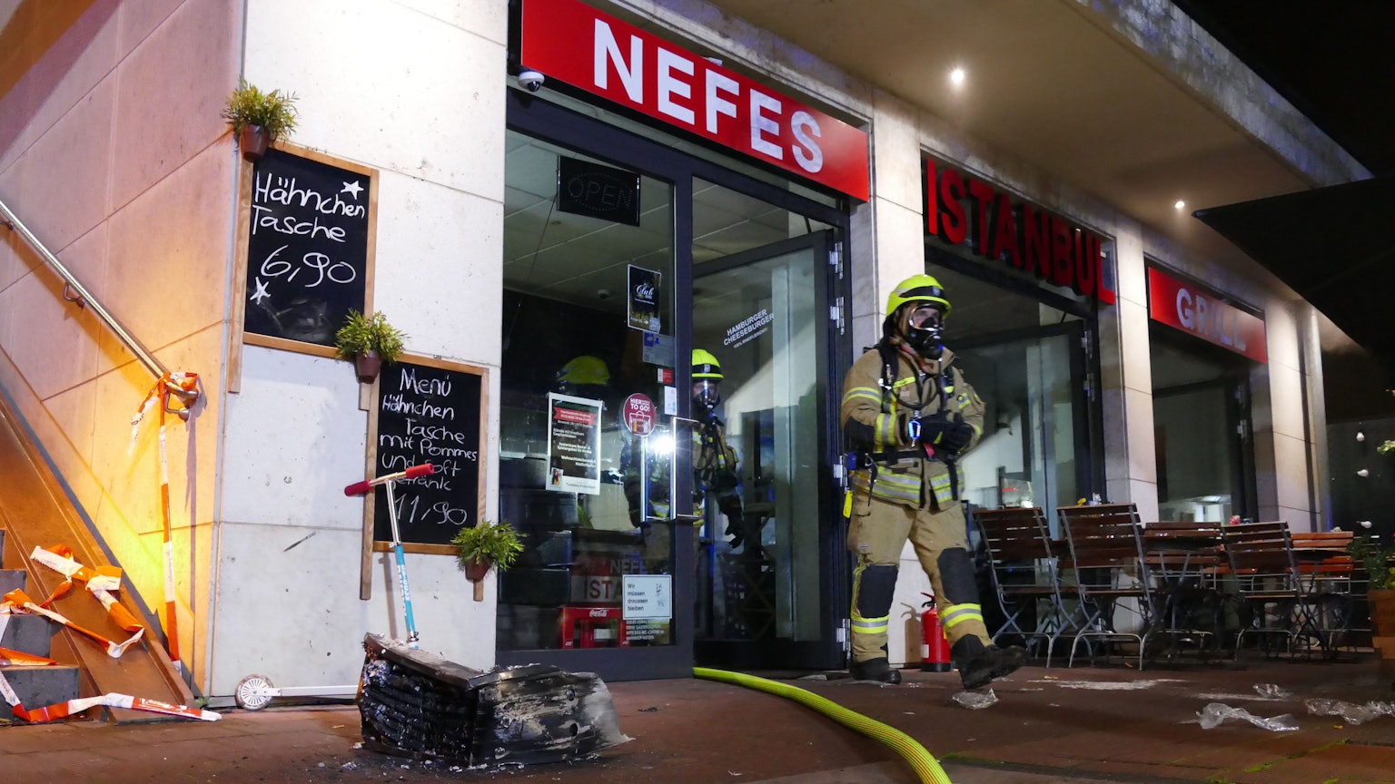 Zwei Feuerwehrmänner mit Atemschutzmaske kommen aus dem Imbiss, in dem es zu dem Brand kam.
