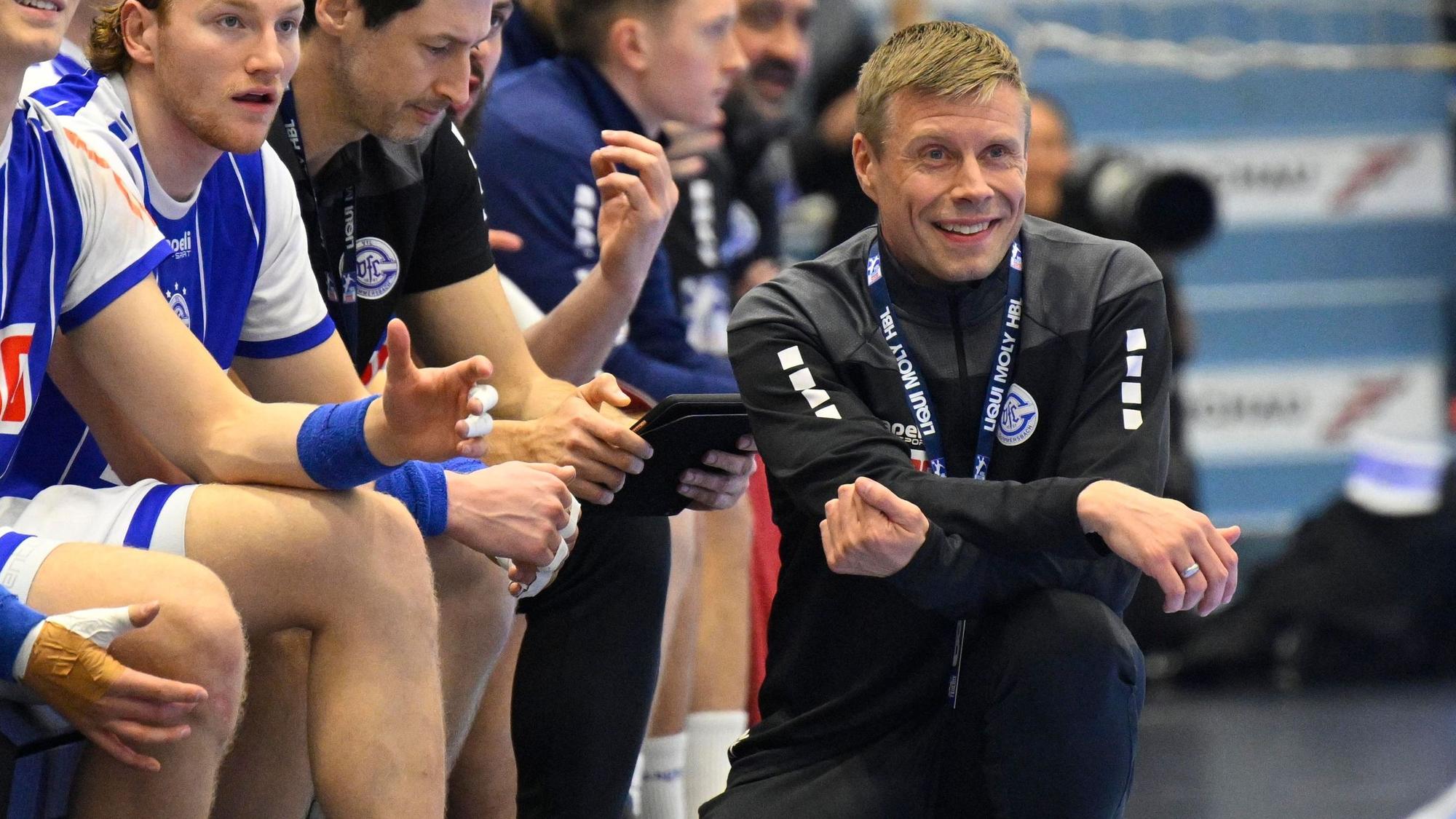 Trainer des Vfl Gummersbach sitzt vor der Bank der Mannschaft in der Hocke.