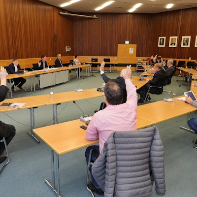 Der Kreisausschuss sitzt im Sitzungssaal in Bergisch Gladbach. Die Mitglieder heben die Hand zur Abstimmung, ebenso Landrat Stephan Santelmann.