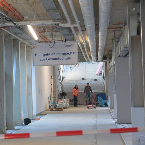Ein noch im Bau befindlicher Flur im Rösrather Schulzentrun, an dessen Ende zwei Arbeiter stehen. An der Decke hängt ein Schild mit der Aufschrift "Hier geht es demnächst zur Gesamtschule".