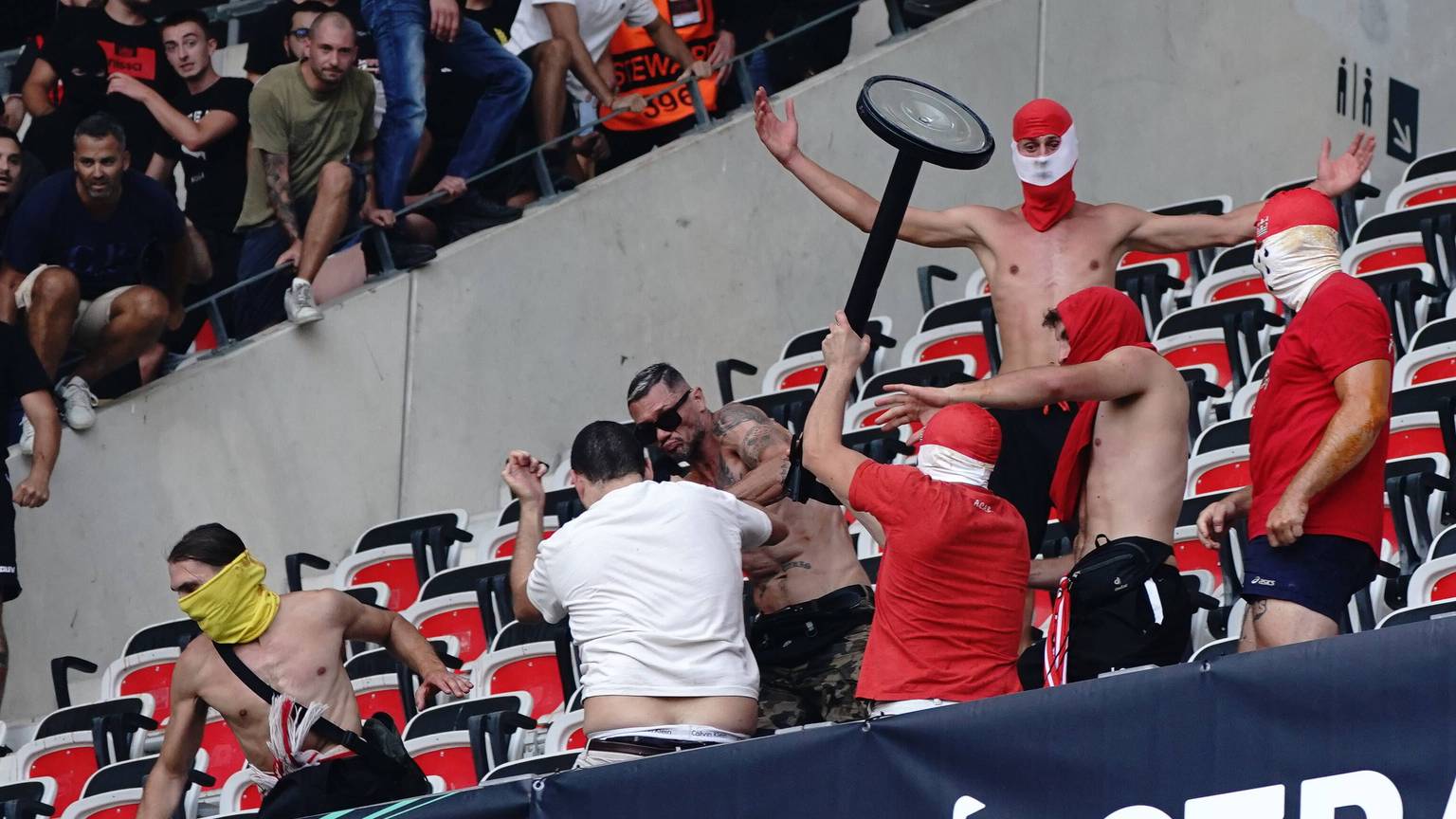 Ein Hooligan schlägt mit einem Gegenstand mit anderen Randalieren auf einen am Boden liegenden Mann ein.