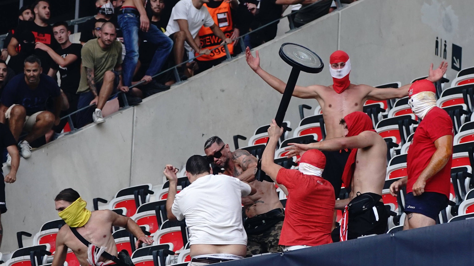 Ein Hooligan schlägt mit einem Gegenstand mit anderen Randalieren auf einen am Boden liegenden Mann ein.