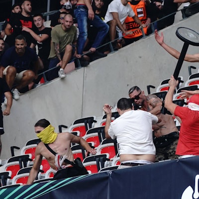 Ein Hooligan schlägt mit einem Gegenstand mit anderen Randalieren auf einen am Boden liegenden Mann ein.