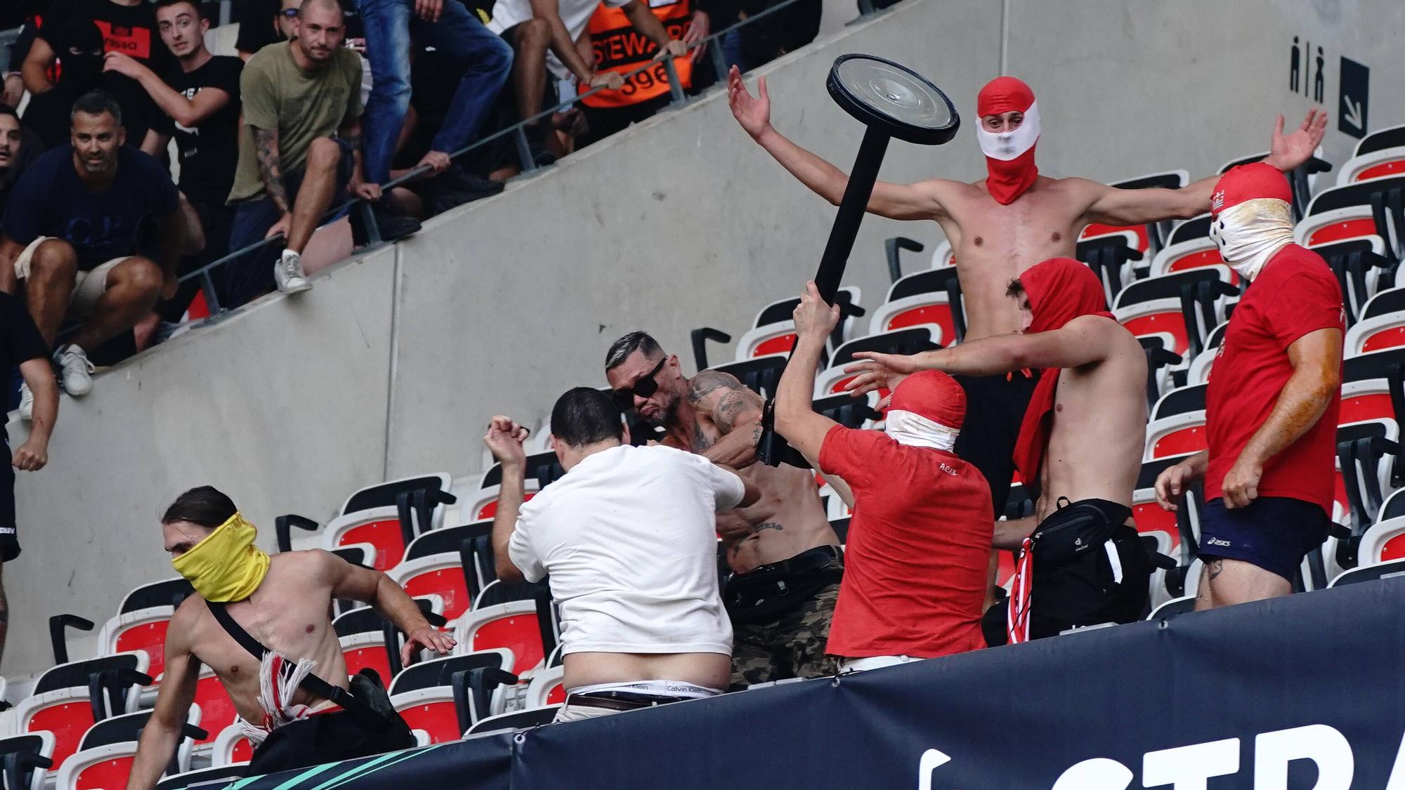 Ein Hooligan schlägt mit einem Gegenstand mit anderen Randalieren auf einen am Boden liegenden Mann ein.