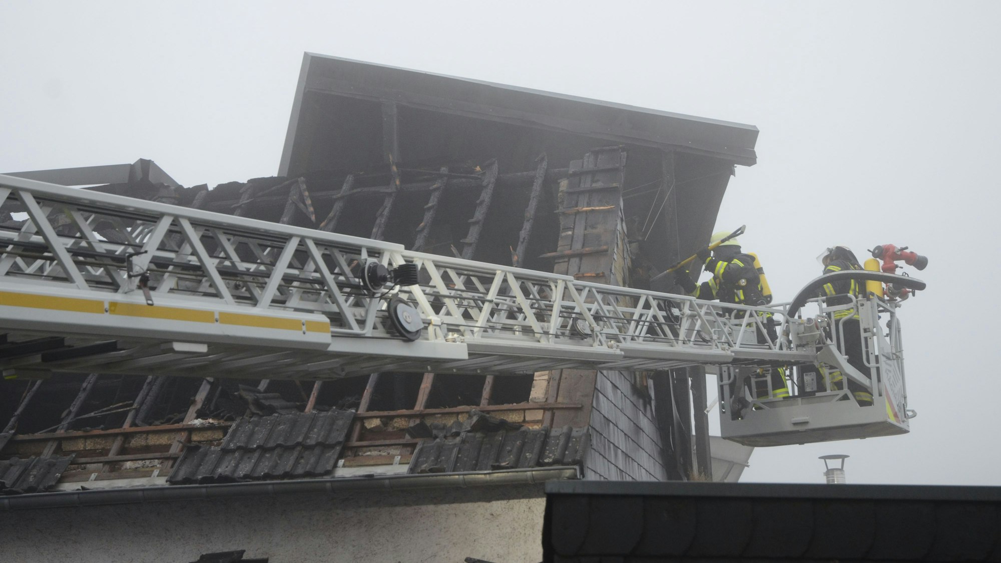 Feuerwehrleute öffnen vom Korb der Drehleiter aus die Fassade des Hauses.