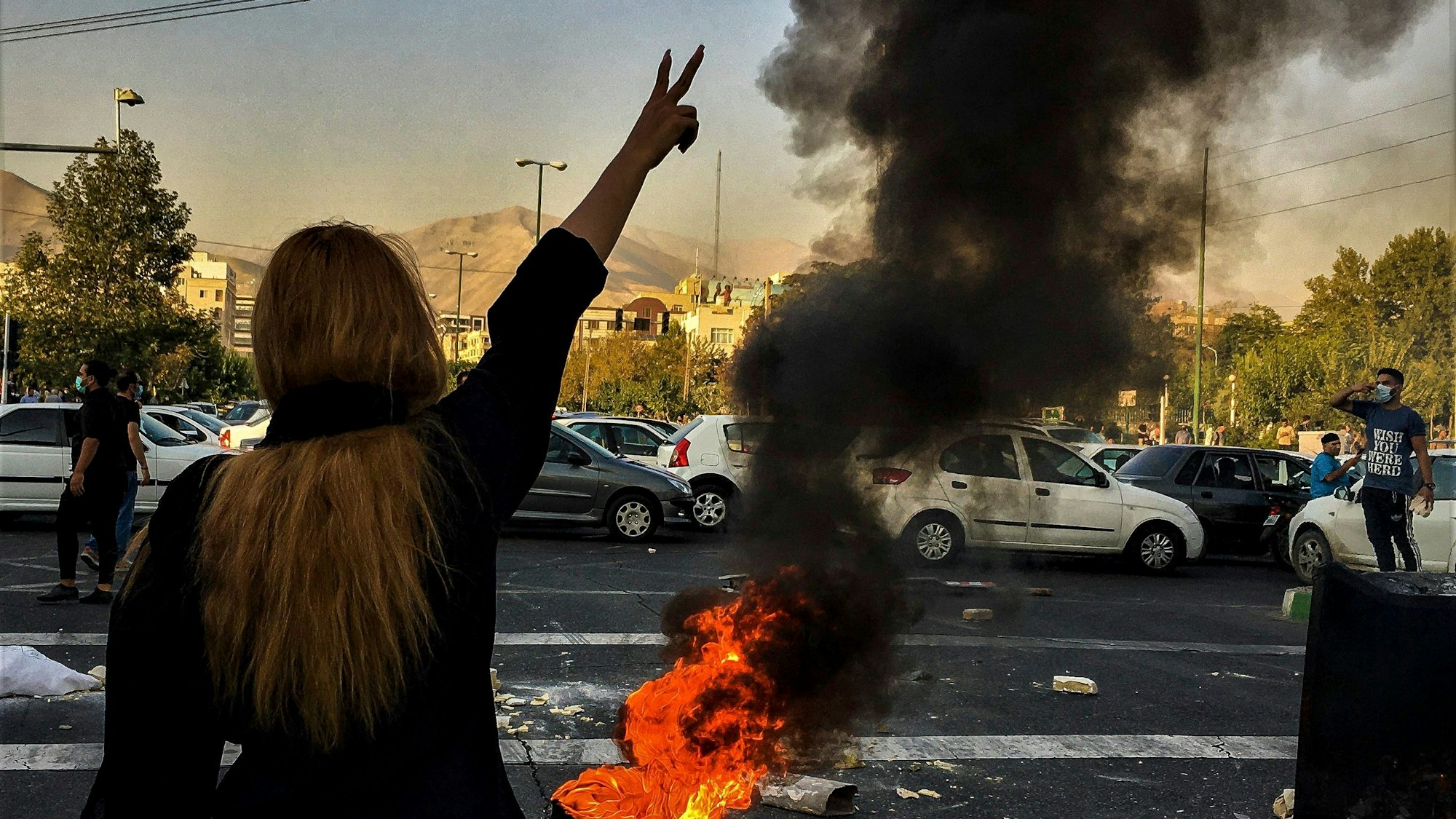 Eine Frau steht während einer Demonstration nach dem Tod der 22-jährigen Mahsa Amini vor einem brennenden Autoreifen und zeigt das Victory-Zeichen.