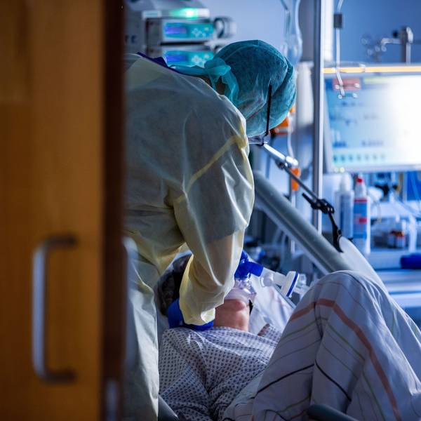 Ein Pfleger kümmert sich in Schutzausrüstung um eine Patientin, die beatmet wird.