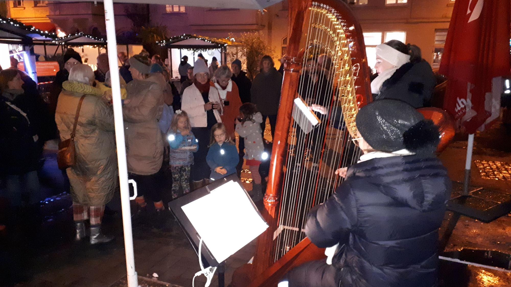Eine Frau spielt auf der Harfe, Erwachsene und Kinder sehen ihr zu. Im Hintergrund ist auch der Nikolaus zu sehen.