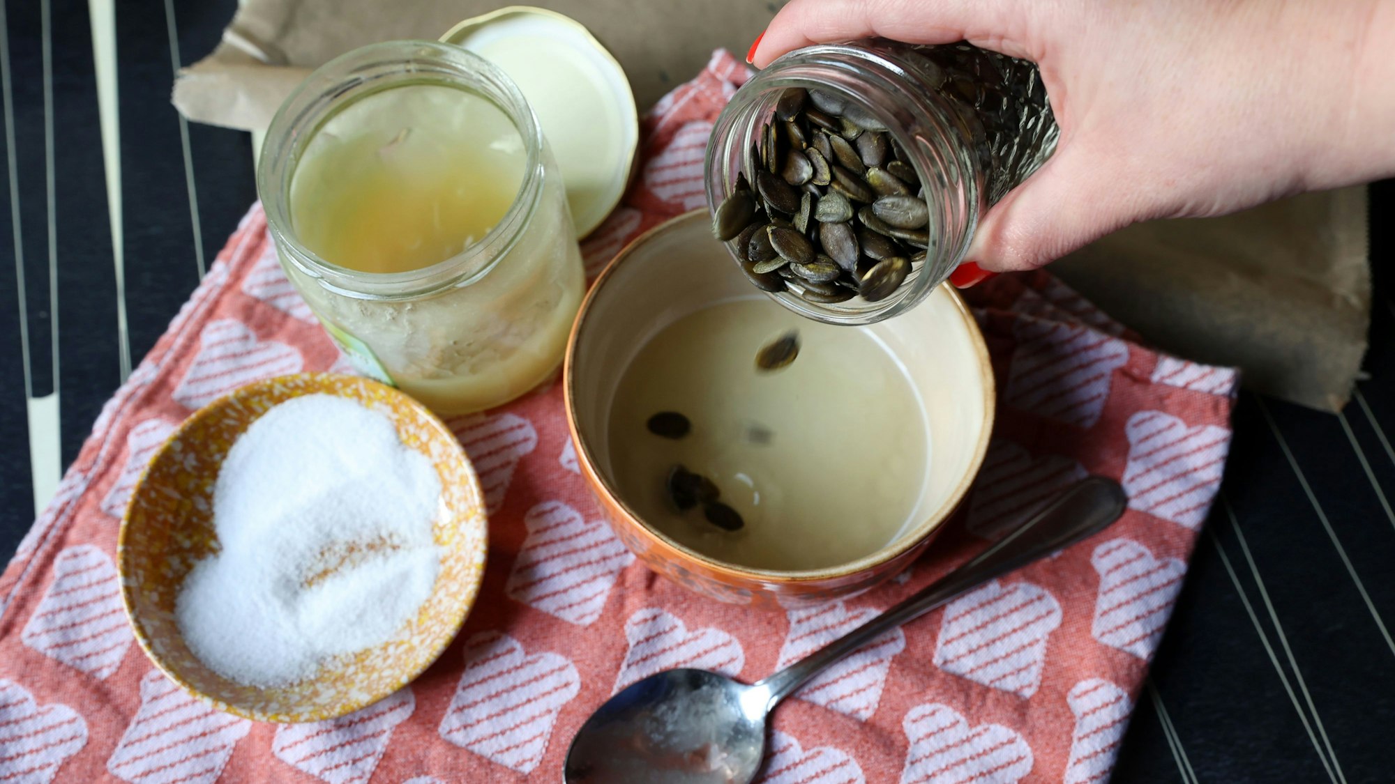 Julia Floß schüttet Kürbiskerne in eine vorbereitete Flüssigkeit aus Honig, Wasser und Salz.