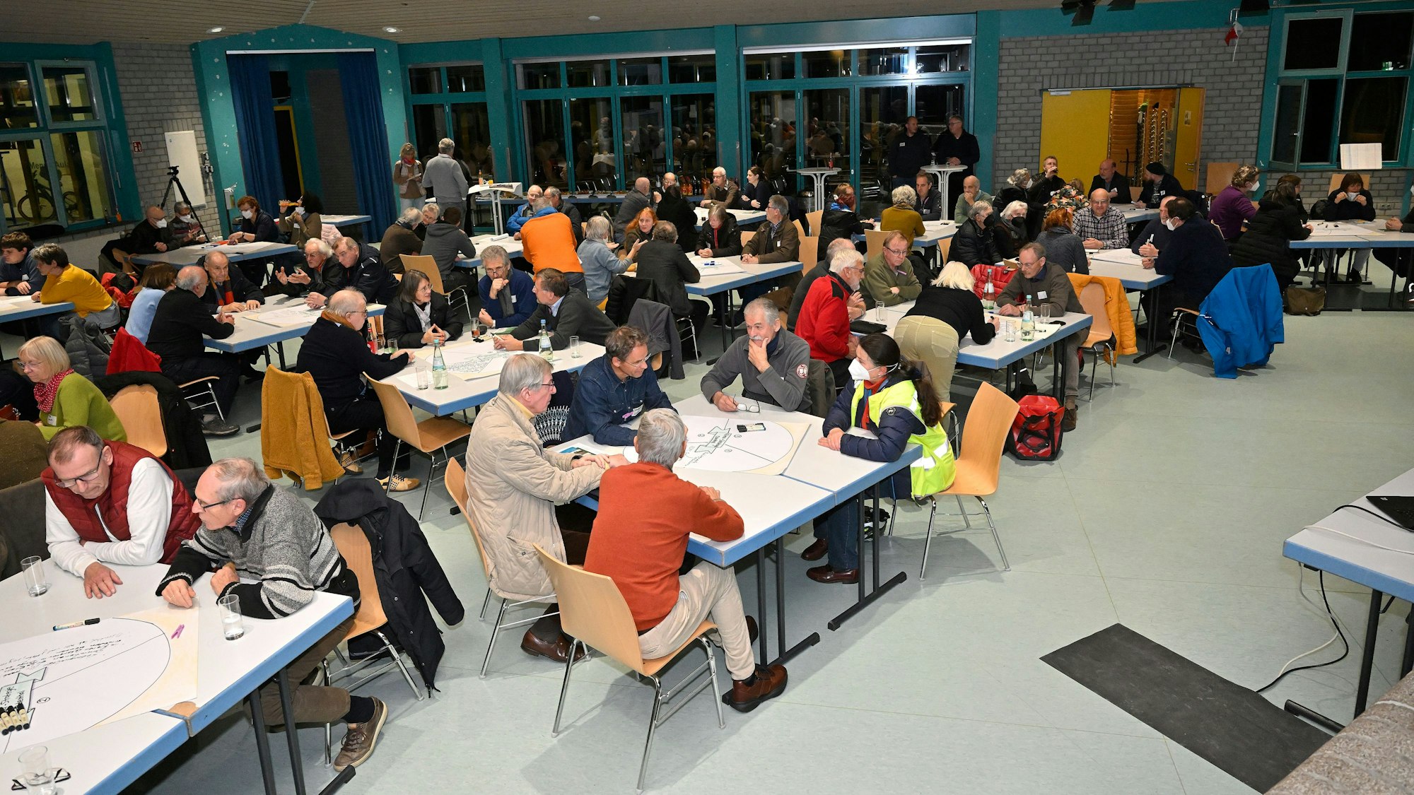 Viele Menschen sitzen an Tischen und unterhalten sich.