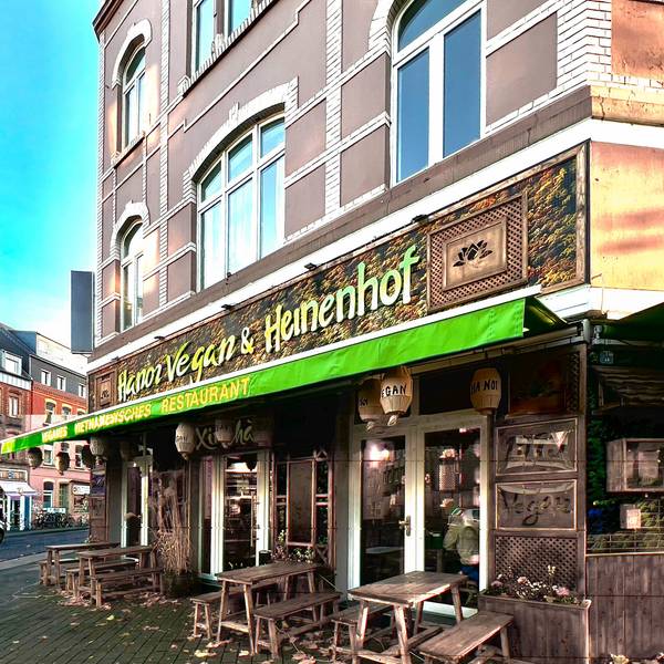 Eine grüne Markise hängt an einem Eckhaus, das eine asiatisch anmutende Fassade mit Holzornamenten hat.