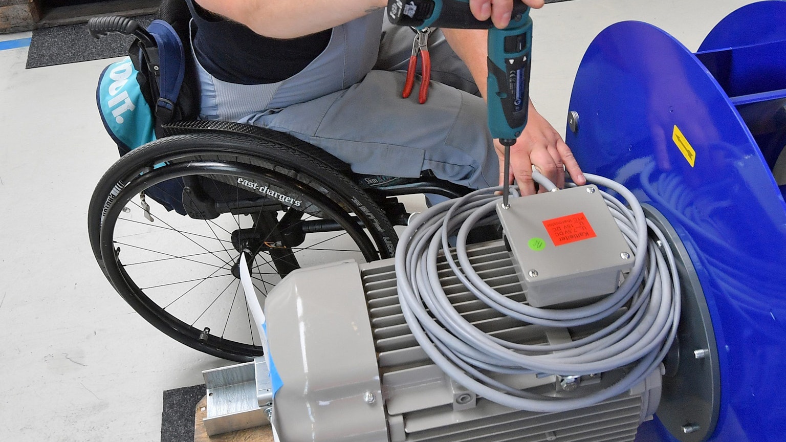 An einem Arbeitsplatz ist ein Mitarbeiter im Rollstuhl mit Montagearbeiten beschäftigt.
