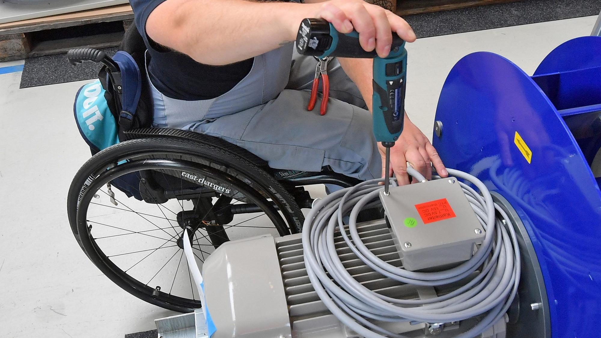 An einem Arbeitsplatz ist ein Mitarbeiter im Rollstuhl mit Montagearbeiten beschäftigt.
