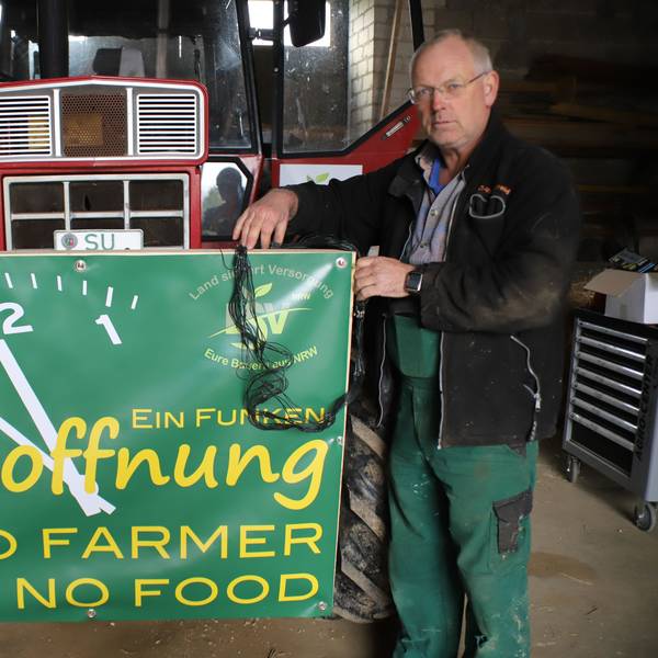 Ein Landwirt steht mit einem Protestschild vor einem Traktor.