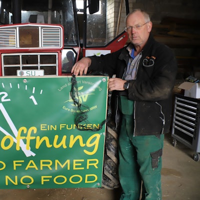 Ein Landwirt steht mit einem Protestschild vor einem Traktor.