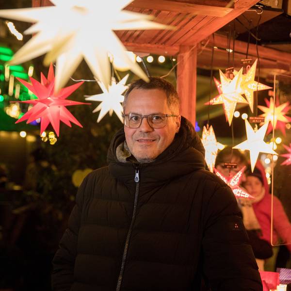Mathias Klabunde steht unter leuchtenden Sternen auf einem Kölner Weihnachtsmarkt.