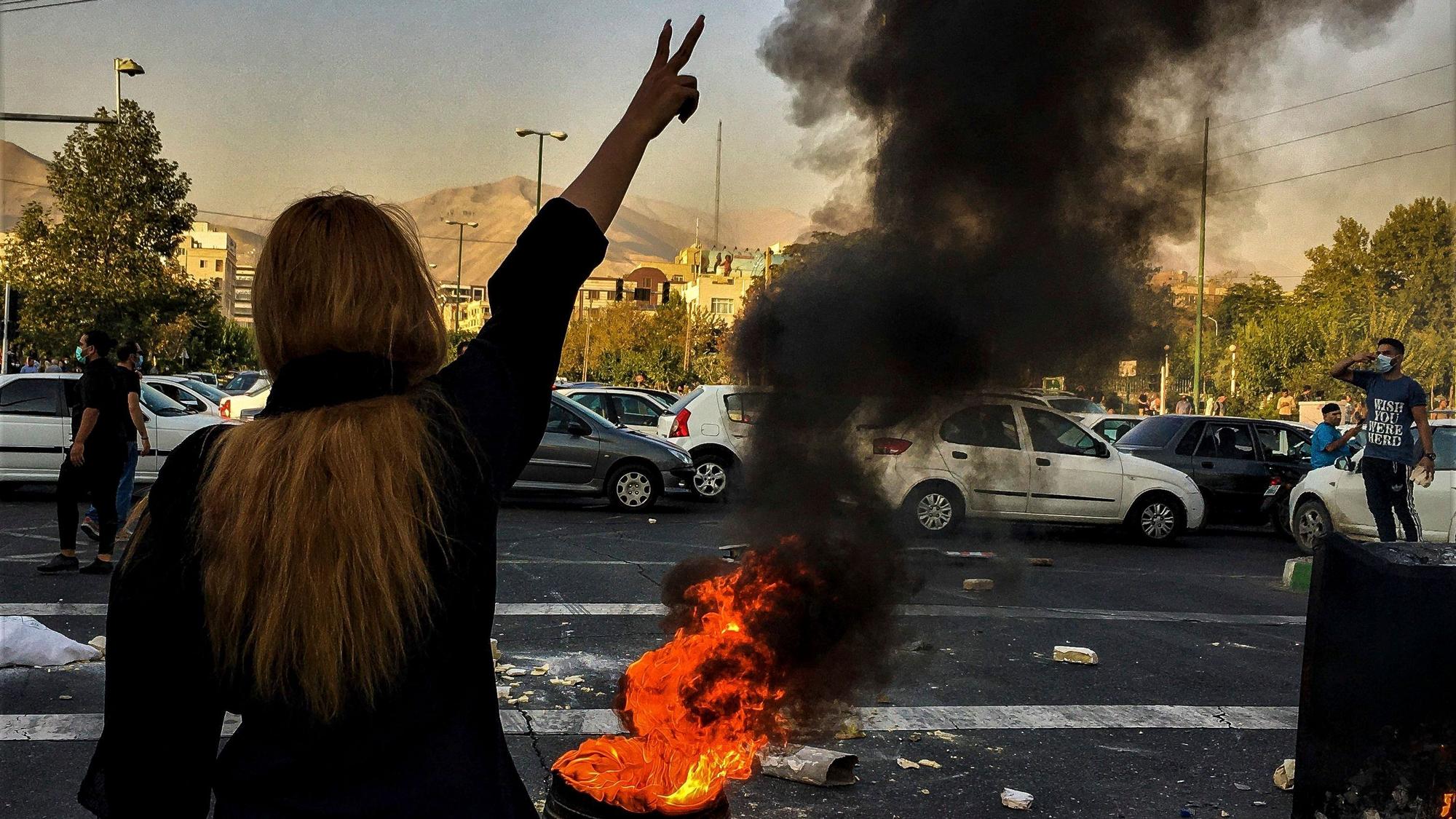 Eine Demonstrantin Teheran steht ohne Kopftuch vor einer brennenden Mülltone.