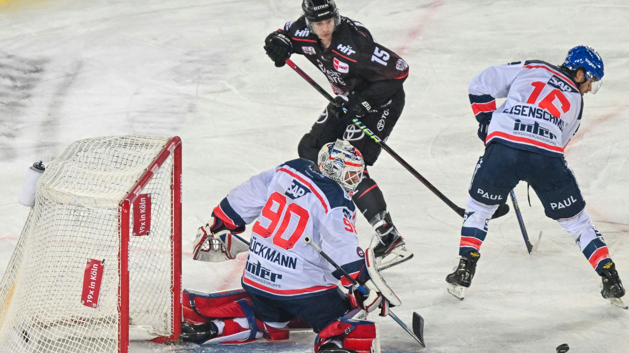 Louis-Marc Aubry Koelner Haie (schwarzes Trikot) beschäftigt Mannheims Torwart Felix Brückmann und Markus Eisenschmid (r.).