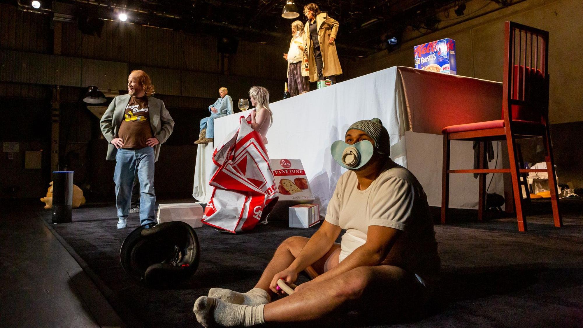 Das Riesenbaby (Paul Basonga) sitzt im Depot des Kölner Schauspiels im Stück „Vor Sonnenaufgang“ in einer XXL-Kulisse.