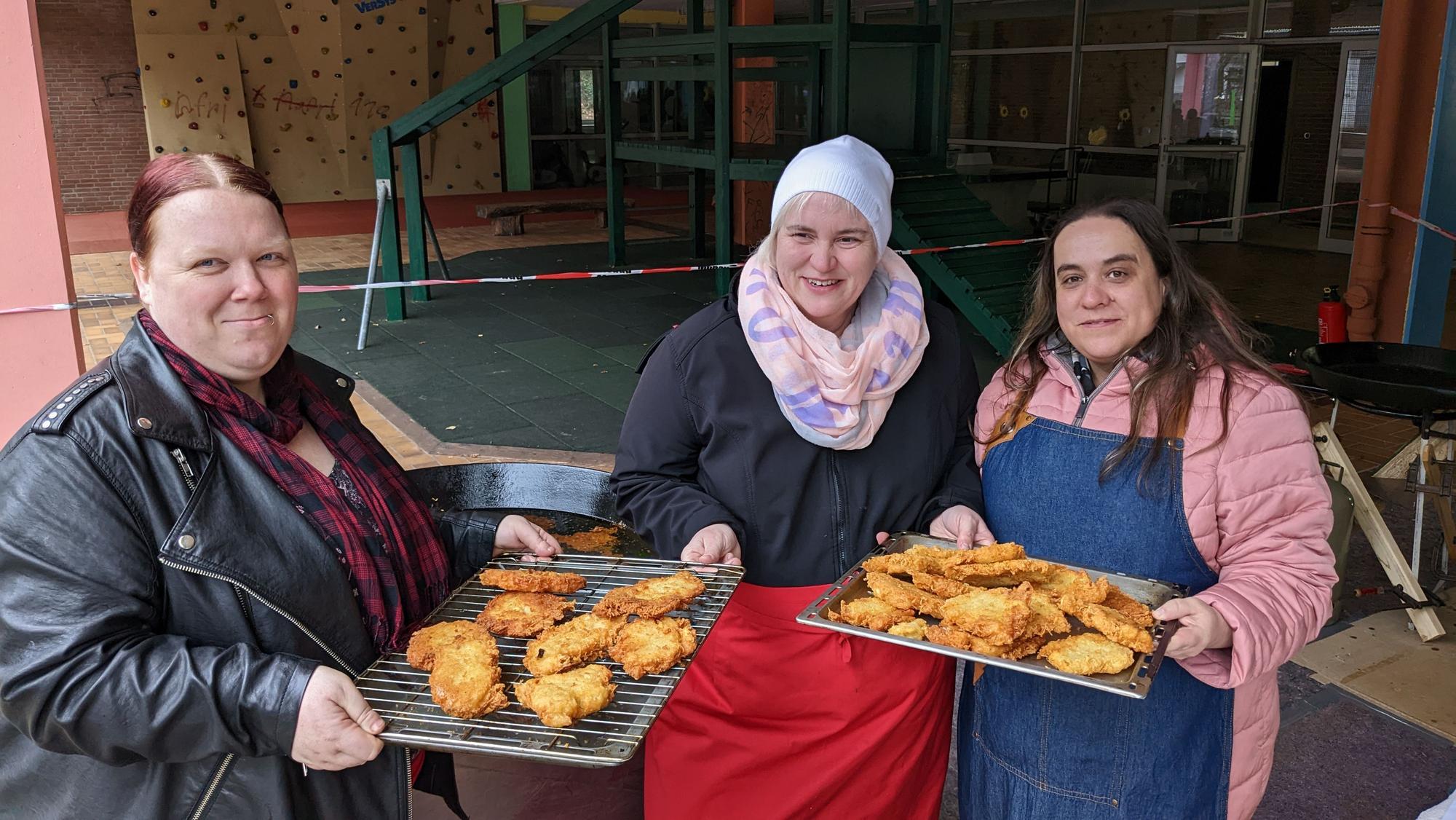 Drei Mütter halten Bleche mit frischen Reibekuchen in den Händen.