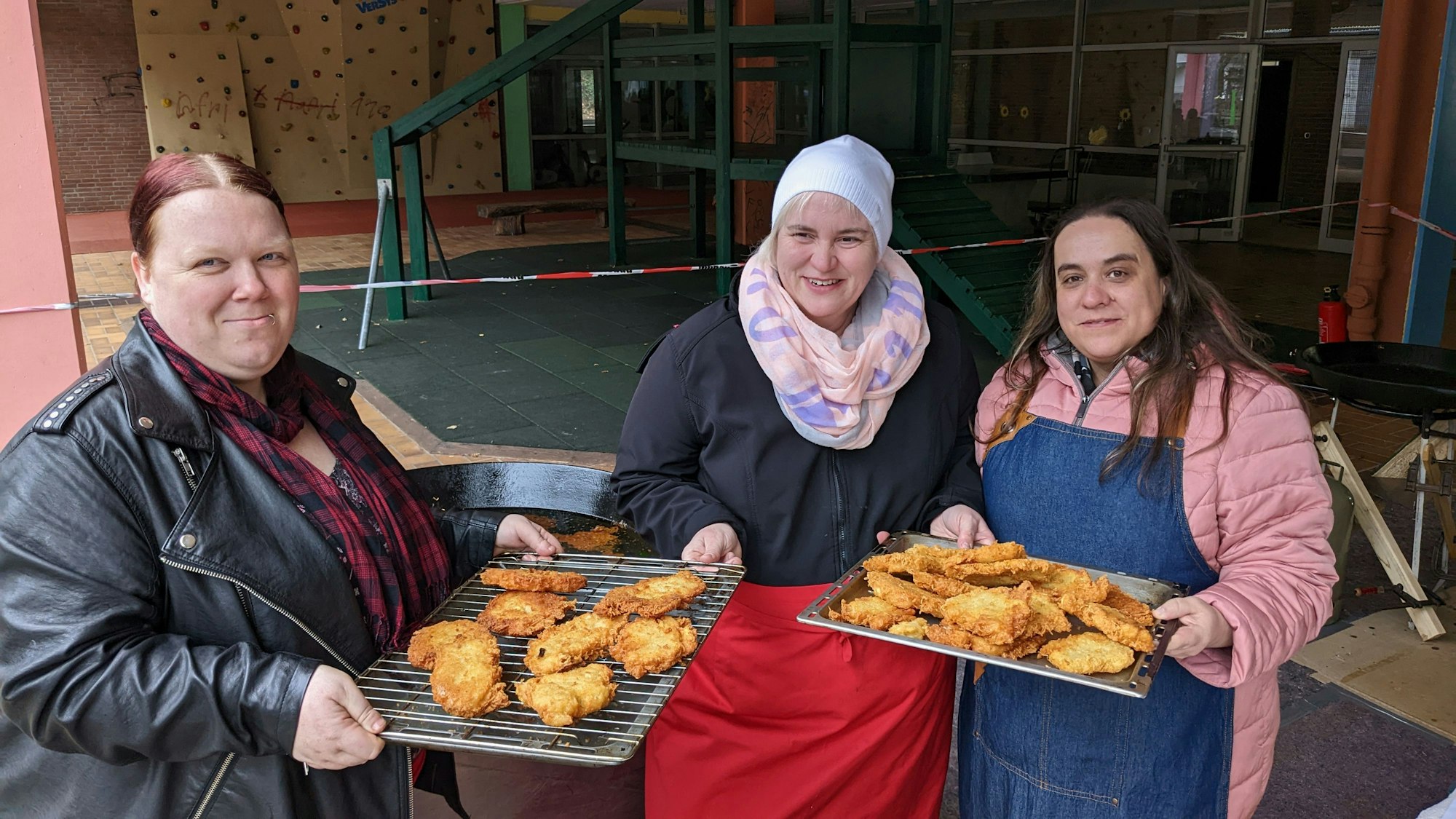 Drei Mütter halten Bleche mit frischen Reibekuchen in den Händen.