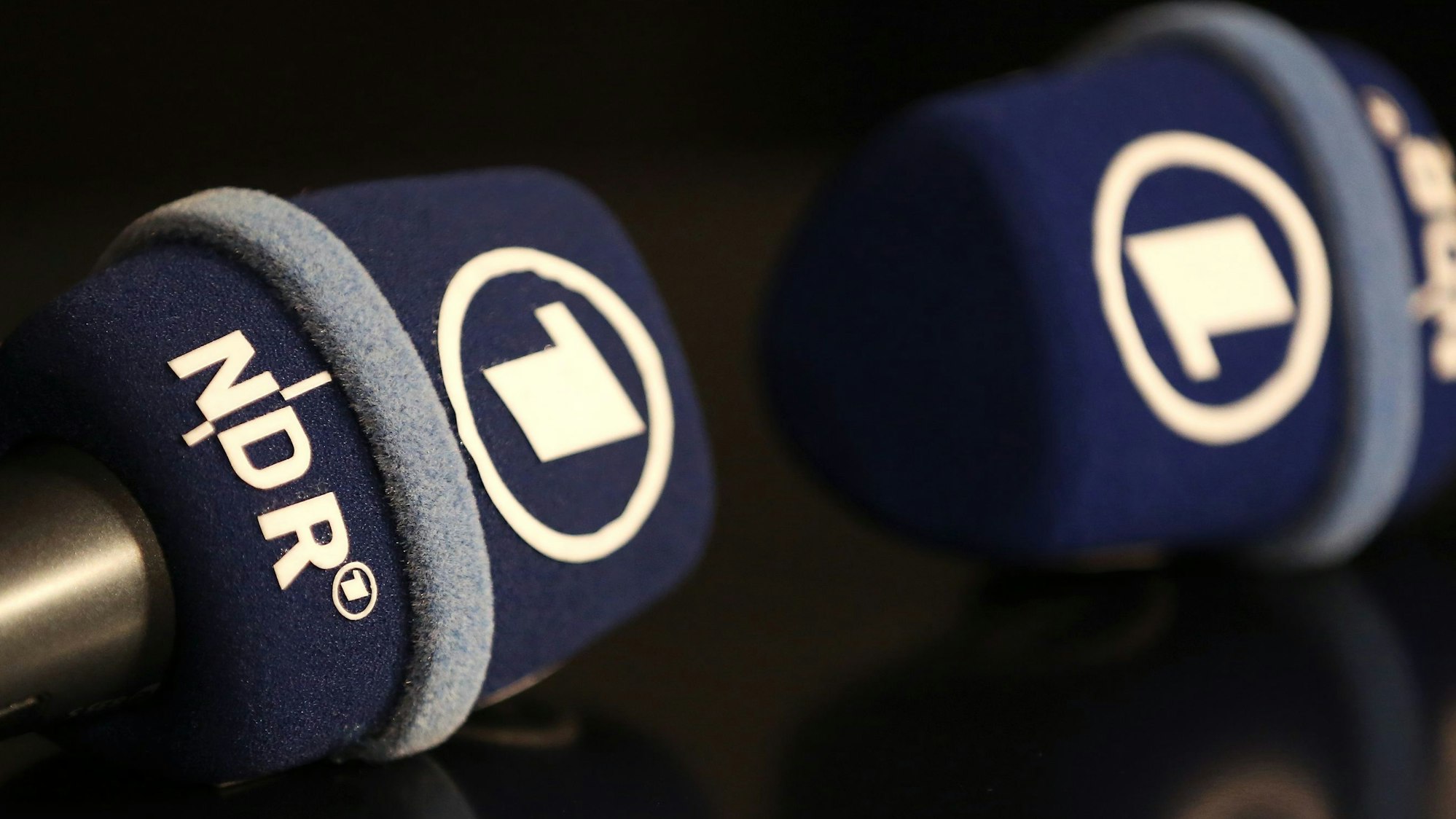 Mikrofone mit dem Logo des Norddeutschen Rundfunks (NDR) und der ARD liegen auf einem Tisch.