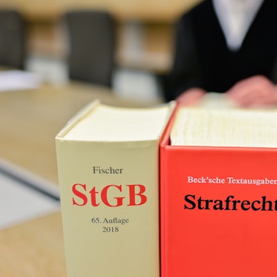 Ein Richter sitzt in einem Sitzungssaal hinter Büchern mit der Aufschrift ´„StGB“ und ´„Strafrecht“.