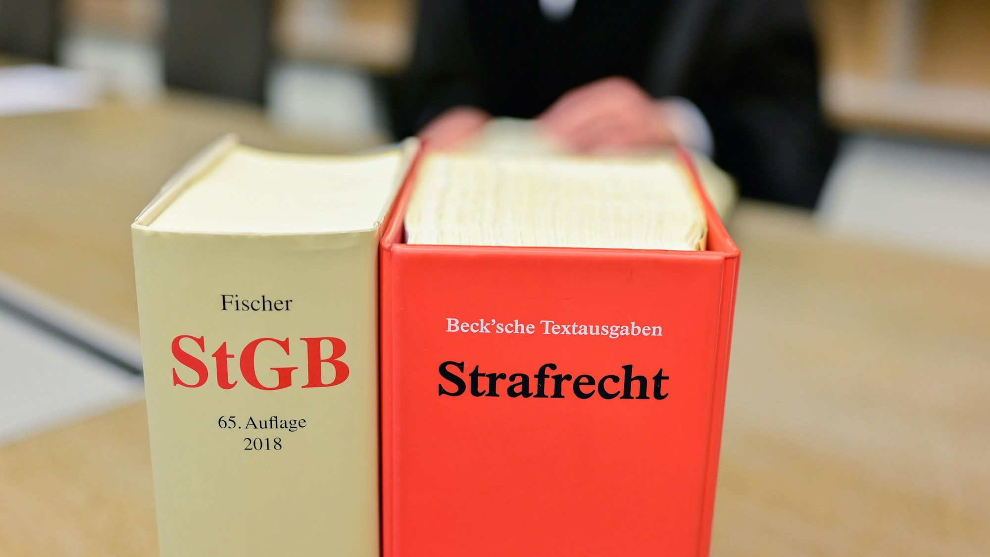 Ein Richter sitzt in einem Sitzungssaal hinter Büchern mit der Aufschrift ´„StGB“ und ´„Strafrecht“.