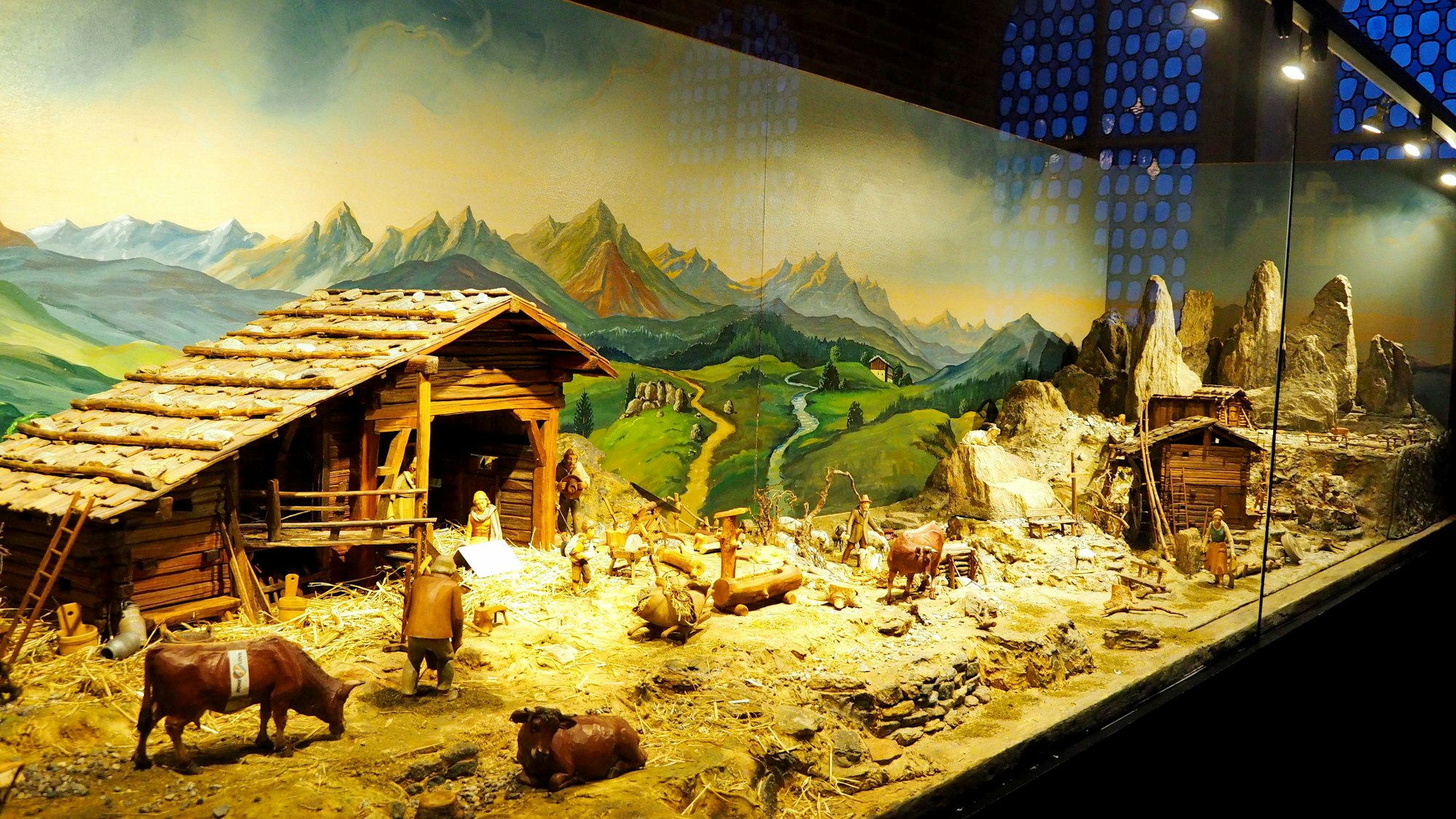 Eine Krippen-Landschaft mit Stall, gemaltem Berg-Panorama im Hintergrnd, Kühen und Menschen ist zu sehen.